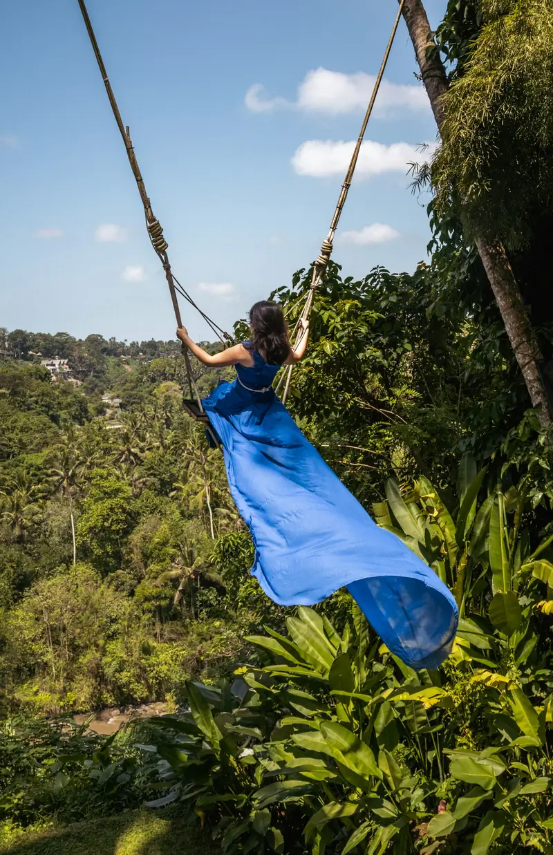 A traveller in a long blue dress on a swing in Bali